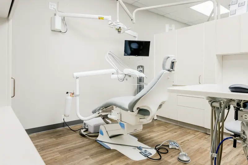 An empty dental treatment room with a chair and instrument tray, and no people